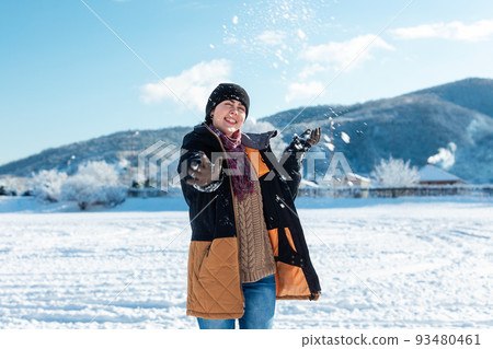 A happy young woman in winter clothes throws a snowball in a snowy park. Mountains in the background. Christmas holidays A happy young woman in winter clothes throws a snowball in a snowy park. Mountains in the background. Christmas holidays 93480461