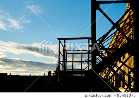 Fire escape on the wall of a yellow brick house against a blue sky with clouds Fire escape on the wall of a yellow brick house against a blue sky with clouds 93481073