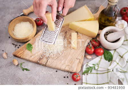 Woman grates Parmesan cheese on a wooden cutting board at domestic kitchen 93481930