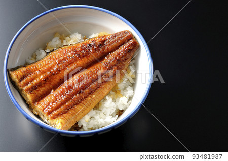 A simple eel bowl with eel kabayaki on top of white rice, taken from above with a black background 93481987