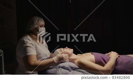 Woman receiving anti-ageing facial massage in spa salon relax. Wellness body skin care face beauty treatment. Black background Woman receiving anti-ageing facial massage in spa salon relax. Wellness body skin care face beauty treatment. Black background 93482800