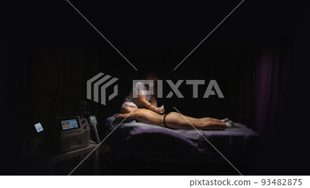 Woman receiving anti-ageing anti-cellulite massage vacuum rf lifting in spa salon. Wellness body and skin care. Black dark background Woman receiving anti-ageing anti-cellulite massage vacuum rf lifting in spa salon. Wellness body and skin care. Black dark background 93482875
