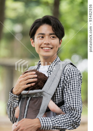 一個年輕的父親把他的孩子抱在背帶裡 一個年輕的父親把他的孩子抱在背帶裡 93482936