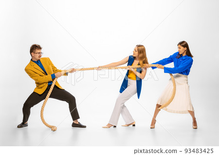 Portrait of two women pulling rope with man symbolizing professional battle, competition isolated over white studio background Portrait of two women pulling rope with man symbolizing professional battle, competition isolated over white studio background 93483425
