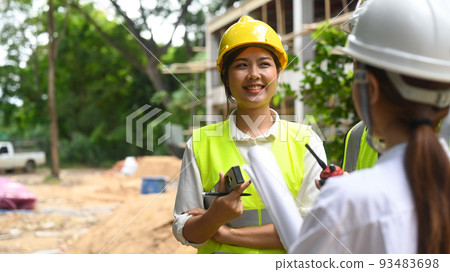 Smiling female engineer supervisor and investor wearing safety helmets discussing the construction process together while visiting a new building Smiling female engineer supervisor and investor wearing safety helmets discussing the construction process together while visiting a new building 93483698