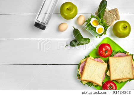 Lunch. Green plate with sandwiches and fresh vegetables, bottle of water and green apple on wooden table. Healthy eating concept. Top view 93484868