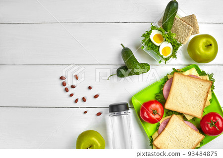 Lunch. Sandwich and fresh vegetables, bottle of water, nuts and fruits on white wooden background. Healthy eating concept. Top view with copy space 93484875