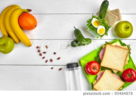 Lunch. Sandwich and fresh vegetables, bottle of water, nuts and fruits on white wooden background. Healthy eating concept. Top view with copy space 93484878