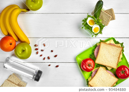 Lunch. Sandwich and fresh vegetables, bottle of water, nuts and fruits on white wooden background. Healthy eating concept. Top view with copy space Lunch. Sandwich and fresh vegetables, bottle of water, nuts and fruits on white wooden background. Healthy eating concept. Top view with copy space 93484880