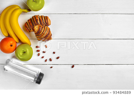 Fruit breakfast with free space on wooden table. Croissant, banana, apple, nuts and a bottle of water. Top view. Fruit breakfast with free space on wooden table. Croissant, banana, apple, nuts and a bottle of water. Top view. 93484889