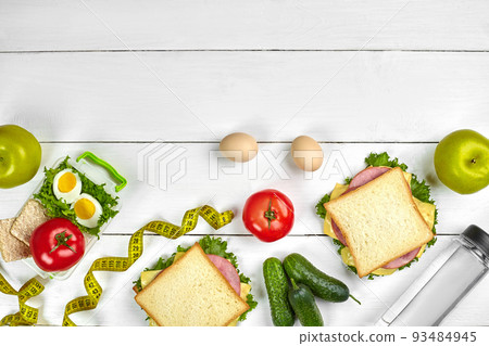 Lunch. Sandwiches and fresh vegetables, bottle of water and green apple on wooden table. Healthy eating concept. Top view Lunch. Sandwiches and fresh vegetables, bottle of water and green apple on wooden table. Healthy eating concept. Top view 93484945