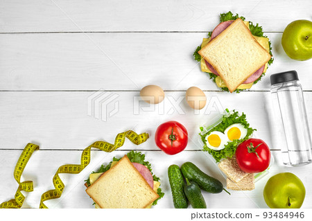 Lunch. Sandwiches and fresh vegetables, bottle of water and green apple on wooden table. Healthy eating concept. Top view Lunch. Sandwiches and fresh vegetables, bottle of water and green apple on wooden table. Healthy eating concept. Top view 93484946