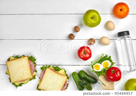Lunch. Sandwich and fresh vegetables, bottle of water, nuts and fruits on white wooden background. Healthy eating concept. Top view with copy space Lunch. Sandwich and fresh vegetables, bottle of water, nuts and fruits on white wooden background. Healthy eating concept. Top view with copy space 93484957