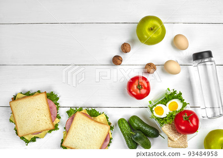 Lunch. Sandwich and fresh vegetables, bottle of water, nuts and fruits on white wooden background. Healthy eating concept. Top view with copy space Lunch. Sandwich and fresh vegetables, bottle of water, nuts and fruits on white wooden background. Healthy eating concept. Top view with copy space 93484958