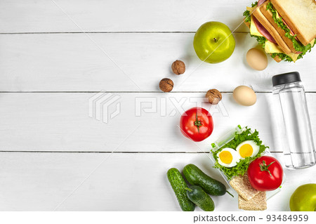 Lunch. Sandwich and fresh vegetables, bottle of water, nuts and fruits on white wooden background. Healthy eating concept. Top view with copy space Lunch. Sandwich and fresh vegetables, bottle of water, nuts and fruits on white wooden background. Healthy eating concept. Top view with copy space 93484959