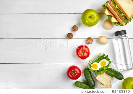 Lunch. Sandwich and fresh vegetables, bottle of water, nuts and fruits on white wooden background. Healthy eating concept. Top view with copy space 93485570
