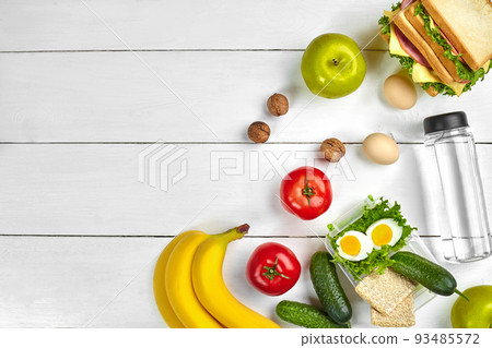 Lunch. Sandwich and fresh vegetables, bottle of water, nuts and fruits on white wooden background. Healthy eating concept. Top view with copy space Lunch. Sandwich and fresh vegetables, bottle of water, nuts and fruits on white wooden background. Healthy eating concept. Top view with copy space 93485572