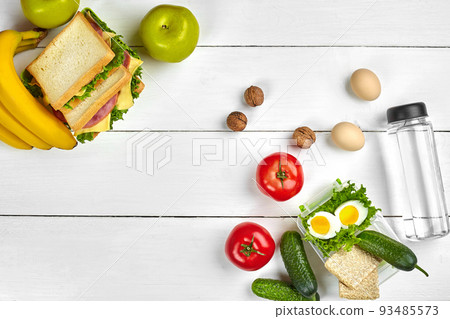 Lunch. Sandwich and fresh vegetables, bottle of water, nuts and fruits on white wooden background. Healthy eating concept. Top view with copy space 93485573
