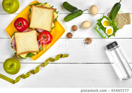 Lunch. Sandwich and fresh vegetables, bottle of water, nuts and fruits on white wooden background. Healthy eating concept. Top view with copy space Lunch. Sandwich and fresh vegetables, bottle of water, nuts and fruits on white wooden background. Healthy eating concept. Top view with copy space 93485577