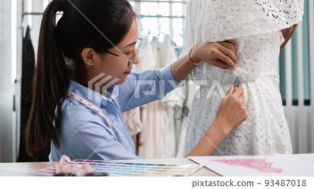 Beautiful young Asian fashion tailor with textile sewing accessories and entrepreneur designer sketches are full of bright colors on the desk with a laptop for creative ideas in the studio Beautiful young Asian fashion tailor with textile sewing accessories and entrepreneur designer sketches are full of bright colors on the desk with a laptop for creative ideas in the studio 93487018