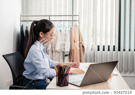 Beautiful young Asian fashion tailor with textile sewing accessories and entrepreneur designer sketches are full of bright colors on the desk with a laptop for creative ideas in the studio Beautiful young Asian fashion tailor with textile sewing accessories and entrepreneur designer sketches are full of bright colors on the desk with a laptop for creative ideas in the studio 93487019