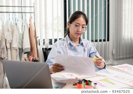 Beautiful young Asian fashion tailor with textile sewing accessories and entrepreneur designer sketches are full of bright colors on the desk with a laptop for creative ideas in the studio Beautiful young Asian fashion tailor with textile sewing accessories and entrepreneur designer sketches are full of bright colors on the desk with a laptop for creative ideas in the studio 93487020