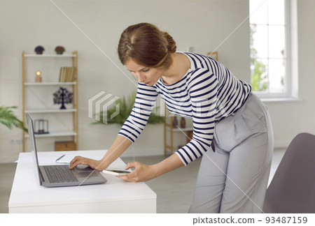 Young business woman standing by office work desk and using laptop and mobile phone Young business woman standing by office work desk and using laptop and mobile phone 93487159