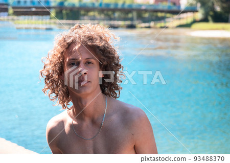 Portrait of a young teen boy with curly wet hair near the river having fun with friends at a summer party. Portrait of a young teen boy with curly wet hair near the river having fun with friends at a summer party. 93488370