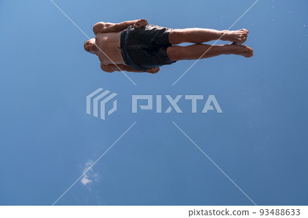 Young teen boy jumping flying and diving in the river. Clear blue sky and trees in distance as a natural background. Young teen boy jumping flying and diving in the river. Clear blue sky and trees in distance as a natural background. 93488633