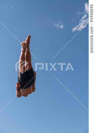 Young teen boy jumping flying and diving in the river. Clear blue sky and trees in distance as a natural background. Young teen boy jumping flying and diving in the river. Clear blue sky and trees in distance as a natural background. 93488848