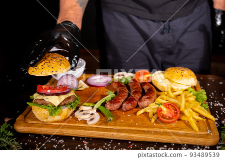 fast food burger potatoes fries sausages cutlets ketchup tomatoes onions peppers mushrooms on a wooden board on the table top view barbecue mix 93489539