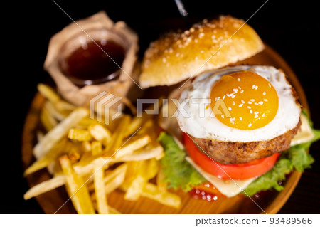 Close-up of beef burger with fried egg on black background. Hamburger - bun, grilled meat burger, lettuce, tomato and fried egg. 93489566