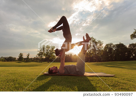 Healthy man lying on grass and balancing woman. Couple doing acrobatic yoga exercise in park Healthy man lying on grass and balancing woman. Couple doing acrobatic yoga exercise in park 93490097