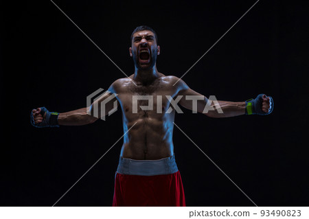 Oriental boxer celebrating his victory with raised arms in black gloves on black background 93490823