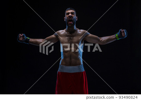 Oriental boxer celebrating his victory with raised arms in black gloves on black background Oriental boxer celebrating his victory with raised arms in black gloves on black background 93490824