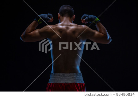 Rear view of strong young male boxer. Fitness male model wearing boxing gloves standing on black background. Rear view of strong young male boxer. Fitness male model wearing boxing gloves standing on black background. 93490834