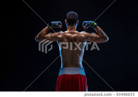 A boxer in his shorts stands with his back on black background. Handsome young bodybuilder with toned body posing shirtless A boxer in his shorts stands with his back on black background. Handsome young bodybuilder with toned body posing shirtless 93490835