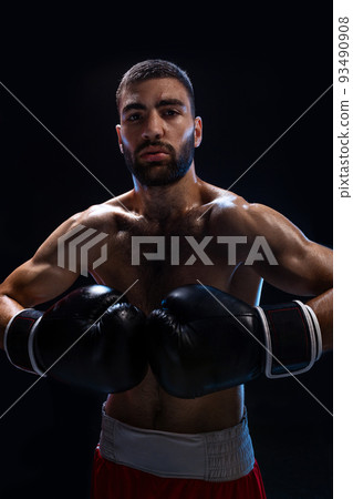 Young male boxer wearing his red boxing shorts and gloves on black background Young male boxer wearing his red boxing shorts and gloves on black background 93490908