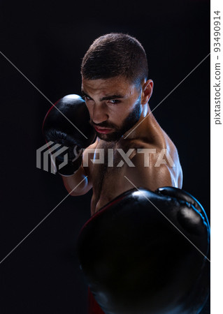 Man is hitting an opponent. Focused fighter with naked torso and boxing gloves looking at the camera. Win. Man is hitting an opponent. Focused fighter with naked torso and boxing gloves looking at the camera. Win. 93490914
