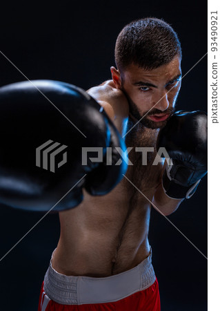 Portrait of tough male boxer posing in boxing stance against black background. 93490921