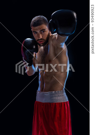 The boxer is ready to deal a powerful blow. Photo of muscular man on black background. The boxer is ready to deal a powerful blow. Photo of muscular man on black background. 93490923