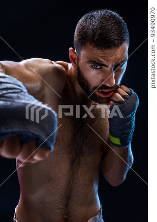 The boxer is ready to deal a powerful blow. Photo of muscular man with strong hands and clenched fists in blue stripes on black background. The boxer is ready to deal a powerful blow. Photo of muscular man with strong hands and clenched fists in blue stripes on black background. 93490970
