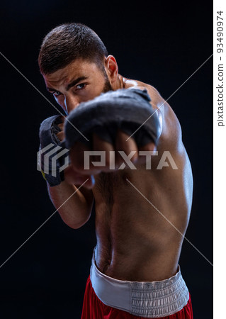The boxer is ready to deal a powerful blow. Photo of muscular man with strong hands and clenched fists in blue stripes on black background. The boxer is ready to deal a powerful blow. Photo of muscular man with strong hands and clenched fists in blue stripes on black background. 93490974