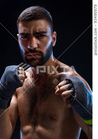 Boxing man ready to fight. Boxer with strong hands and clenched fists in blue straps against a black background 93490979