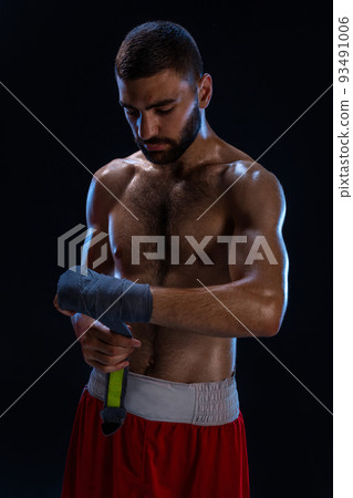 Sports boxer man pulls on the hand wrist wraps. Oriental male model isolated on black background. 93491006