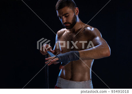 Sports boxer man pulls on the hand wrist wraps. Oriental male model isolated on black background. 93491018