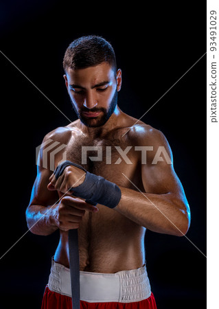 Boxer preparing her gloves for a fight. Photo of muscular man strapping up hands on black background. Boxer preparing her gloves for a fight. Photo of muscular man strapping up hands on black background. 93491029