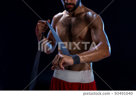 Boxer preparing her gloves for a fight. Photo of muscular man strapping up hands on black background. Boxer preparing her gloves for a fight. Photo of muscular man strapping up hands on black background. 93491040