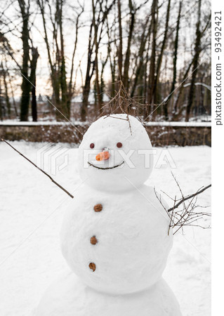 Sloppy tall snowman with carrot nose, walnut buttons stands alone in park field Sloppy tall snowman with carrot nose, walnut buttons stands alone in park field 93492421