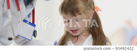 Doctor pediatrician in protective medical mask talking to little girl patient in clinic 93492422